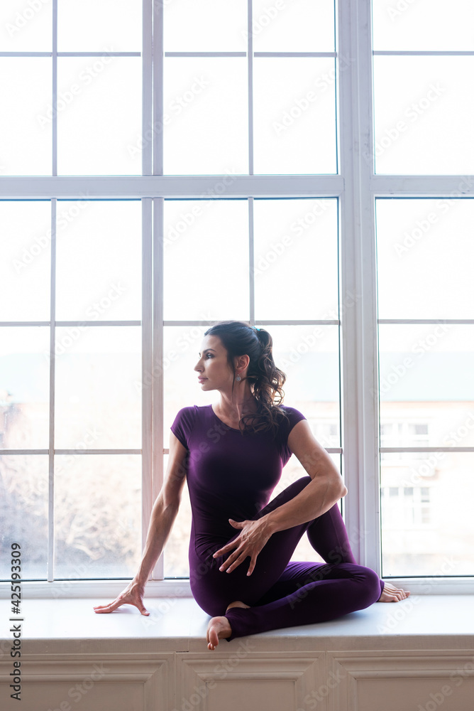 A beautiful dark-haired girl in a sports purple jumpsuit performs yoga asanas. Healthy lifestyle, sports.