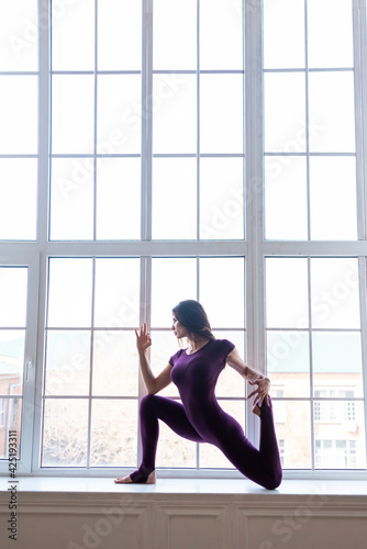 A beautiful dark-haired girl in a sports purple jumpsuit performs yoga asanas. Healthy lifestyle, sports.