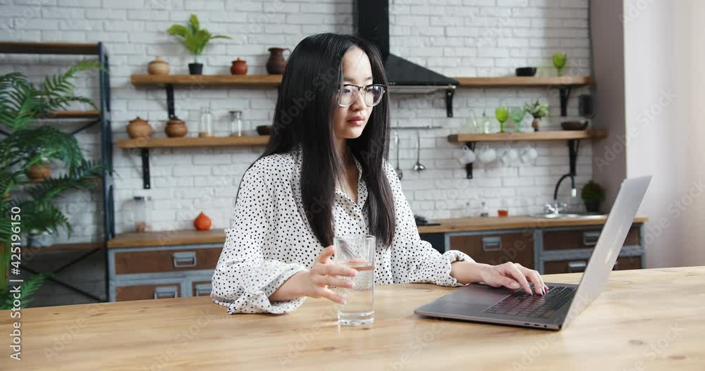 Asian korean woman working at laptop from home living room and drinking water Asian korean woman working at laptop from home living room and drinking water