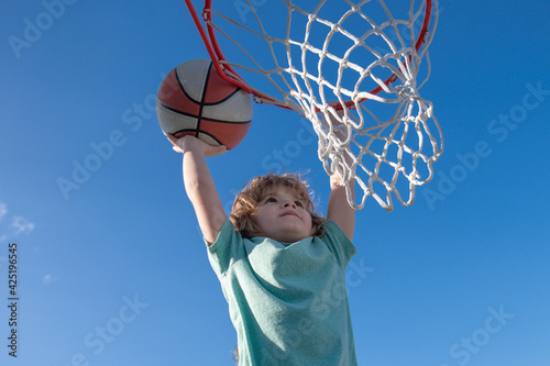 Basketball Slam Dunks of sporty kids basketball player. Close up image of basketball excited kid player dunking the ball, stock photo. Banner isolated on sky background.