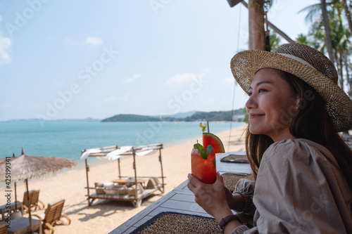 A beautiful young asian woman drinking watermelon juice while sitting in the beach cafe