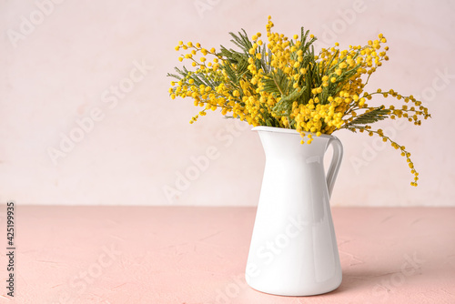 Jug with beautiful mimosa flowers on light background