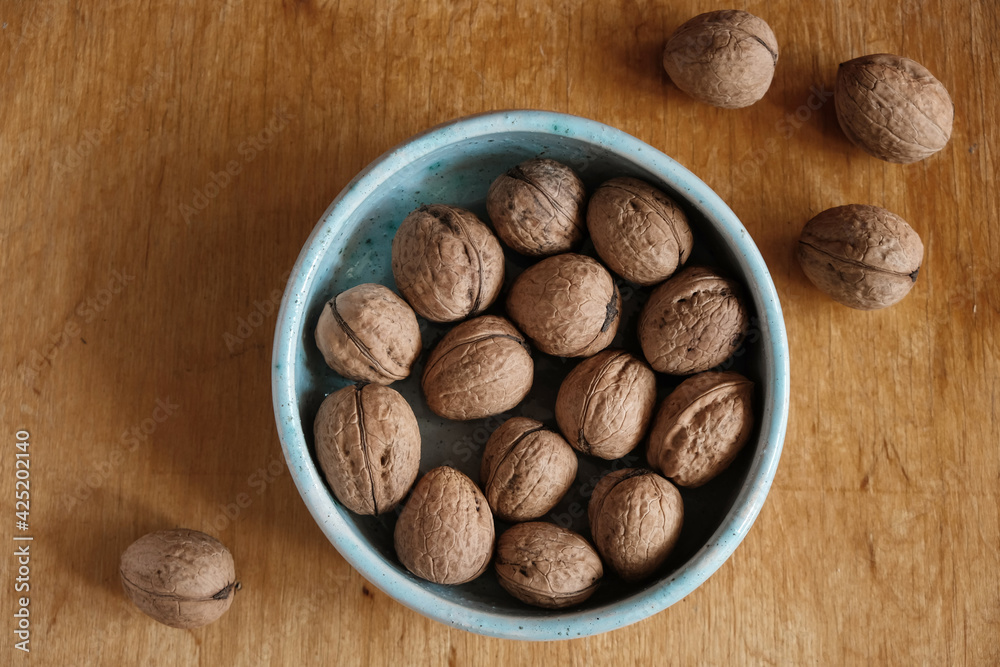 Walnuts in a blue ceramic bowl. Nuts are scattered on a wooden surface. Top view. Walnuts in a blue ceramic bowl. Nuts are scattered on a wooden surface. Top view.