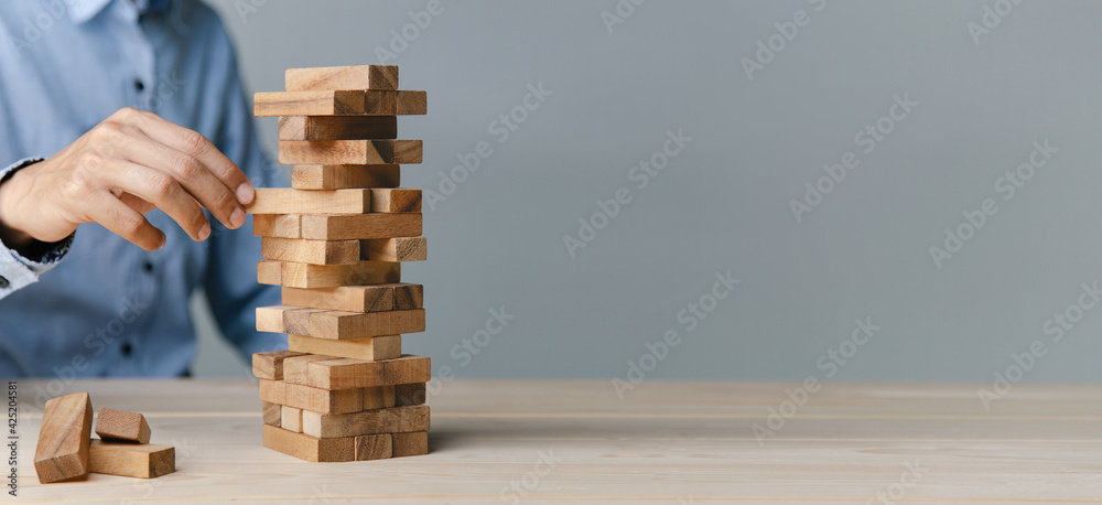 Planning, risk and strategy in business, businessman placing wooden block on a tower.