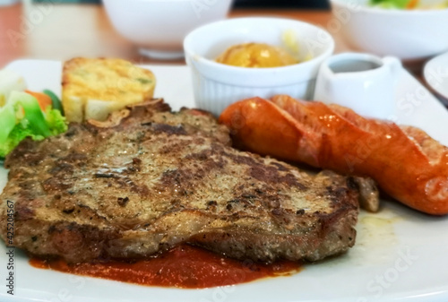 T-bone steak served with crisp sausage, Mashed potatoes, and Garlic bread accompanied by tomato sauce.