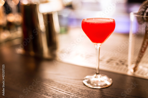 A bright red alcoholic cocktail in a coupe glass at the bar counter. A horizontal lifestyle photo with shallow depth of field and copy space.