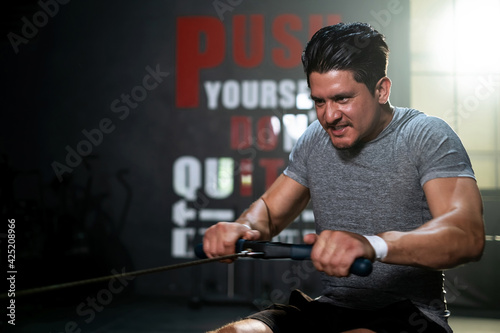 Portrait attractive or athletic man playing rowing machine in the sport fitness gym. Male doing workouts with power exercise machine. Strong motivated muscular. Training and healthy lifestyle.