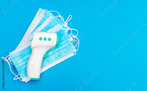 Electronic infrared thermometer with medical masks on blue background. Top view.
