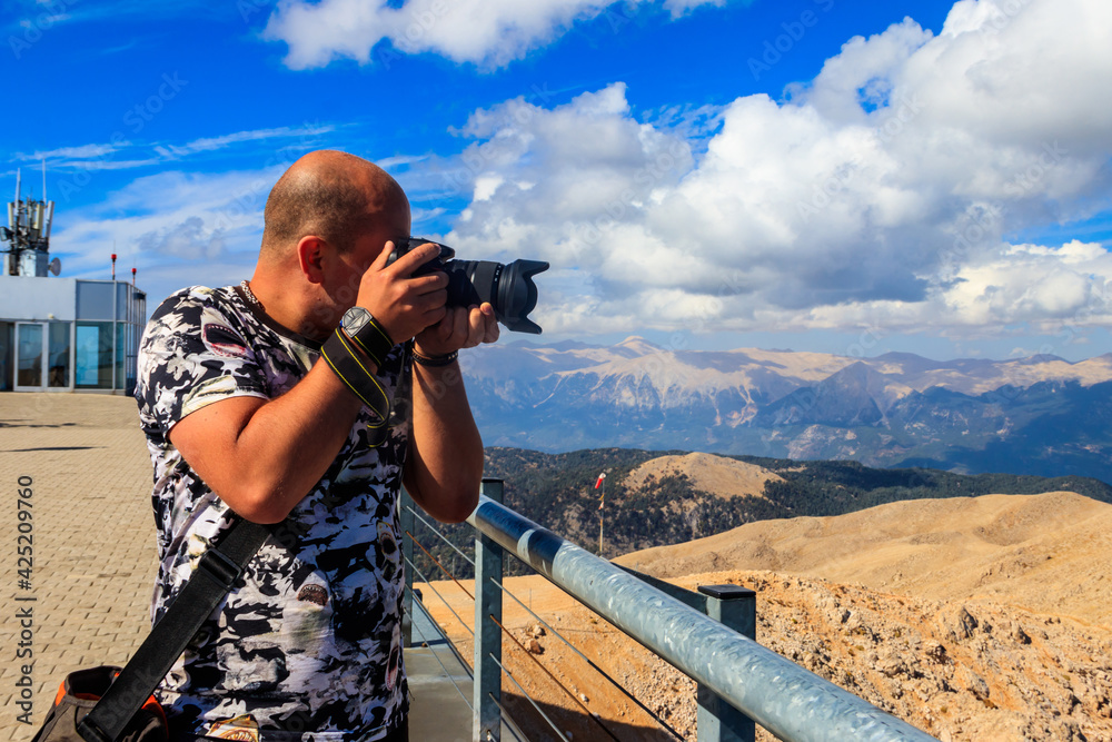 Travel photographer man with professional camera taking photos of  on a top of Tahtali mountain near Kemer, Antalya Province in Turkey