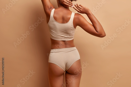фотографія Indoor shot of thin faceless woman stands back to camera demonstrates her ideal