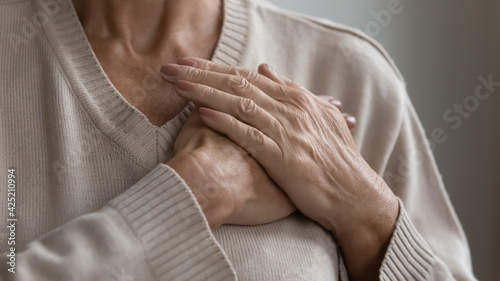 Mature elderly woman feeling heart pain, touching chest with both hands. Thankful senior lady expressing gratitude, love, trust, thanking god, making grateful honor kindness gesture. Close up photo