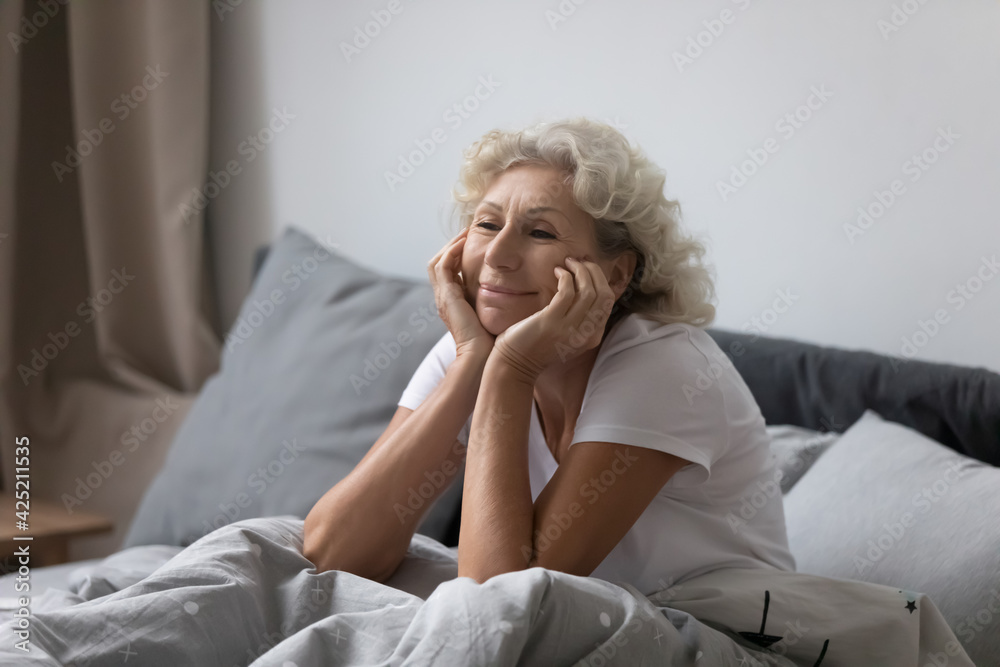 Happy elderly lady awaking in modern comfortable bedroom, sitting on bed and smiling after night of good healthy sleep. Senior mature woman waking up and enjoying vacation morning in hotel room Happy elderly lady awaking in modern comfortable bedroom, sitting on bed and smiling after night of good healthy sleep. Senior mature woman waking up and enjoying vacation morning in hotel room