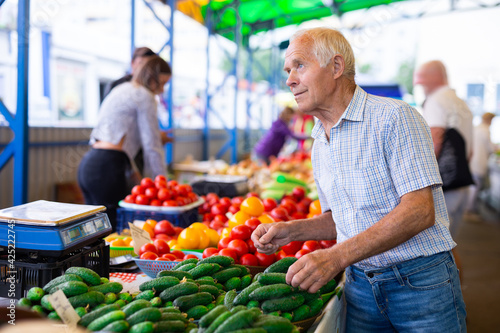 retired european man buys cucumbers and tomatoes in market