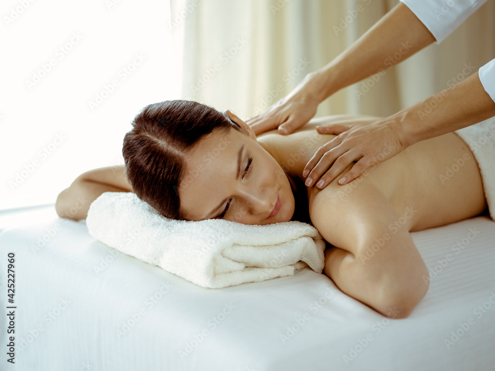 Pretty brunette woman enjoying procedure of back massage in spa salon. Beauty concept