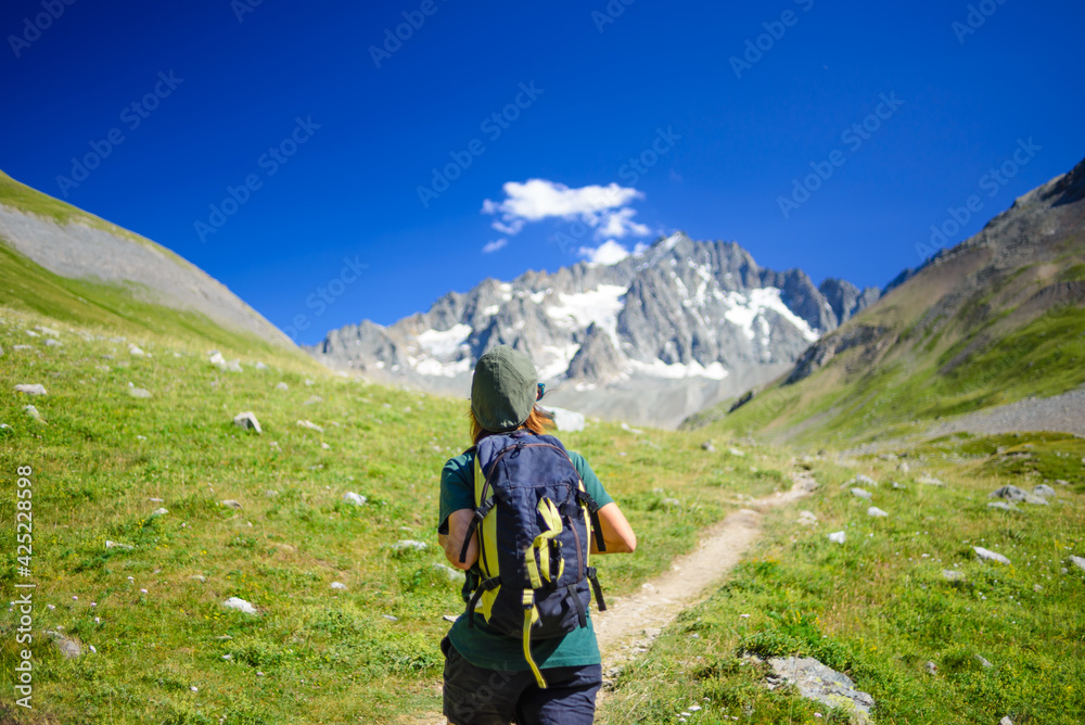 Fototapeta premium Woman with backpack hiking towards mountain top, scenic glacier and dramatic landscape summer fitness wellbeing selective focus rear view, freedom concept
