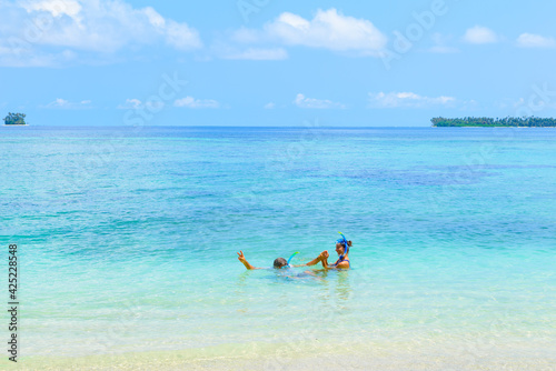 Happy adult couple having fun in turquoise water wearing snorkeling mask. Real people bathing in caribbean sea on tropical beach, islands in the background