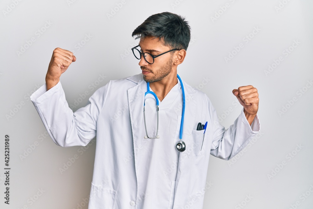 Young handsome man wearing doctor uniform and stethoscope showing arms muscles smiling proud. fitness concept. Young handsome man wearing doctor uniform and stethoscope showing arms muscles smiling proud. fitness concept.
