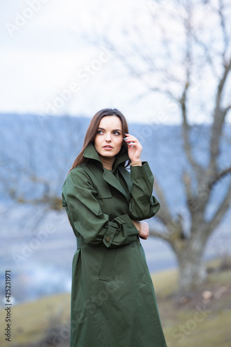 Image of young beautiful woman wearing rain jacket in cold weather. Thinker european girl in spring nature.