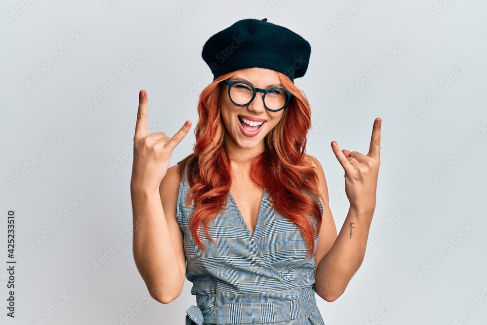 Young redhead woman wearing fashion french look with beret shouting with crazy expression doing rock symbol with hands up. music star. heavy music concept. Young redhead woman wearing fashion french look with beret shouting with crazy expression doing rock symbol with hands up. music star. heavy music concept.