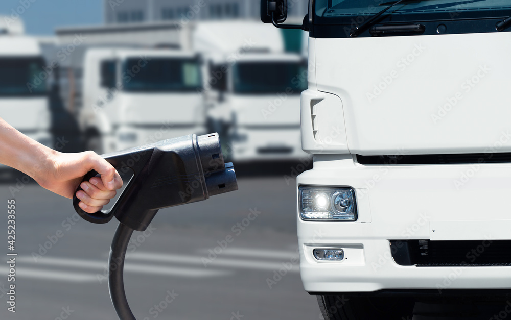 Hand with charging plug on a background of electric truck. Concept	 - obrazy, fototapety, plakaty 