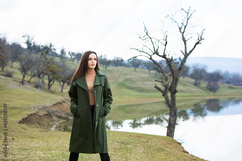 Image of young beautiful woman wearing rain jacket in cold weather. Thinker european girl in spring nature. Image of young beautiful woman wearing rain jacket in cold weather. Thinker european girl in spring nature.