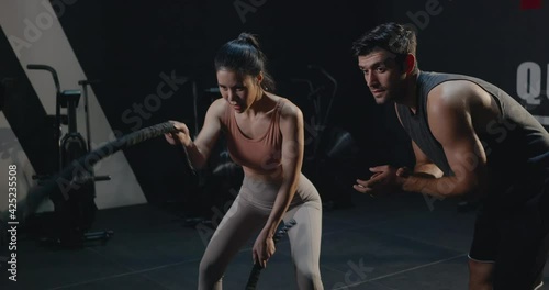 Asian young beautiful woman doing exercise sweat extreme with battle rope in cross fit gym training at club fitness GYM with trainer motivating man, health workout sport trends concept