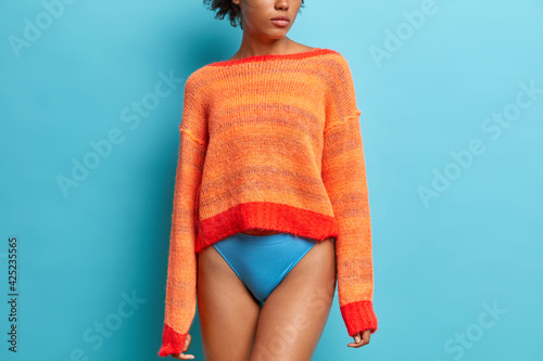 Rear view of slim woman wears long sleeved orange jumper and panties has long legs fit smooth skin fit figure models against blue studio background