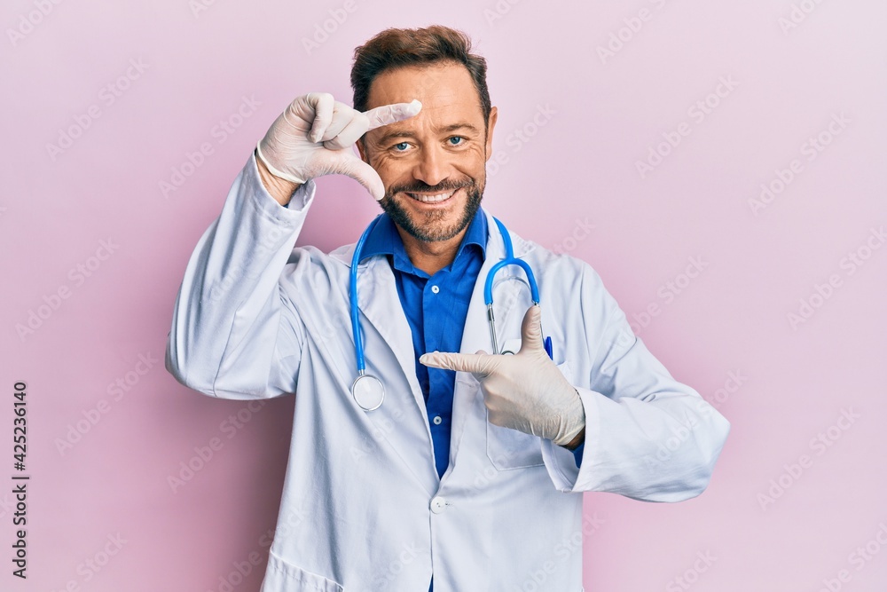Middle age man wearing doctor uniform and stethoscope smiling making frame with hands and fingers with happy face. creativity and photography concept. Middle age man wearing doctor uniform and stethoscope smiling making frame with hands and fingers with happy face. creativity and photography concept.