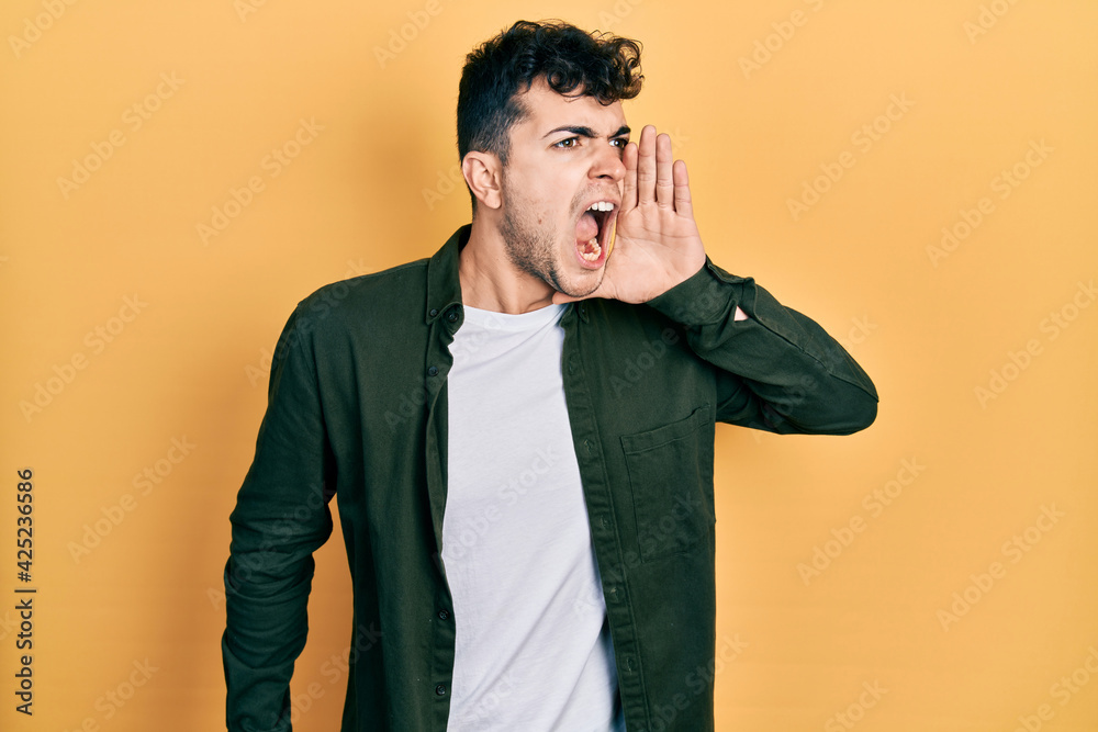 Young hispanic man wearing casual clothes shouting and screaming loud to side with hand on mouth. communication concept. Young hispanic man wearing casual clothes shouting and screaming loud to side with hand on mouth. communication concept.