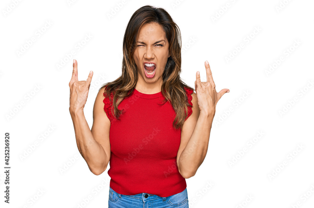 Young hispanic woman wearing casual clothes shouting with crazy expression doing rock symbol with hands up. music star. heavy concept.