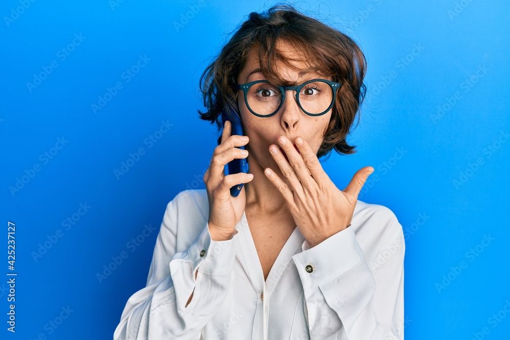 Young brunette woman having conversation talking on the smartphone covering mouth with hand, shocked and afraid for mistake. surprised expression Young brunette woman having conversation talking on the smartphone covering mouth with hand, shocked and afraid for mistake. surprised expression