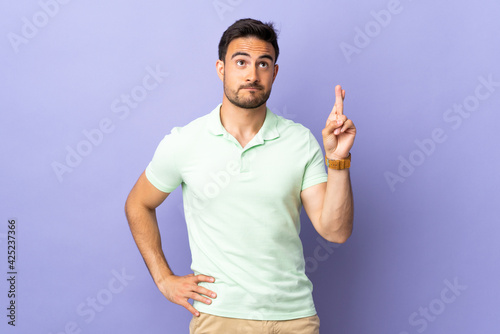 Young handsome man isolated on purple background with fingers crossing and wishing the best