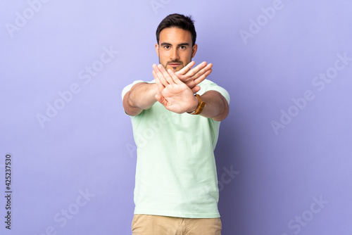 Young handsome man isolated on purple background making stop gesture with her hand to stop an act