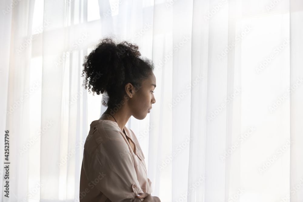 Pensive upset young African American woman look in window distance thinking or pondering. Thoughtful millennial biracial female outcast feel lonely troubled at home. Loner, solitude concept. Pensive upset young African American woman look in window distance thinking or pondering. Thoughtful millennial biracial female outcast feel lonely troubled at home. Loner, solitude concept.