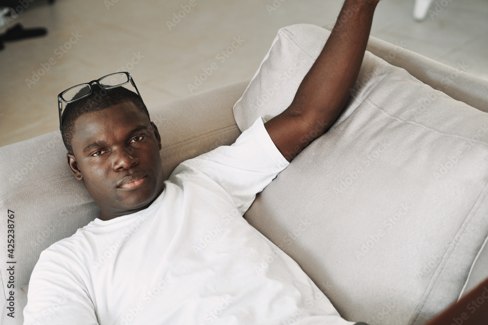 Obraz premium an african man lies on a sofa with glasses on his head and a white t-shirt top view