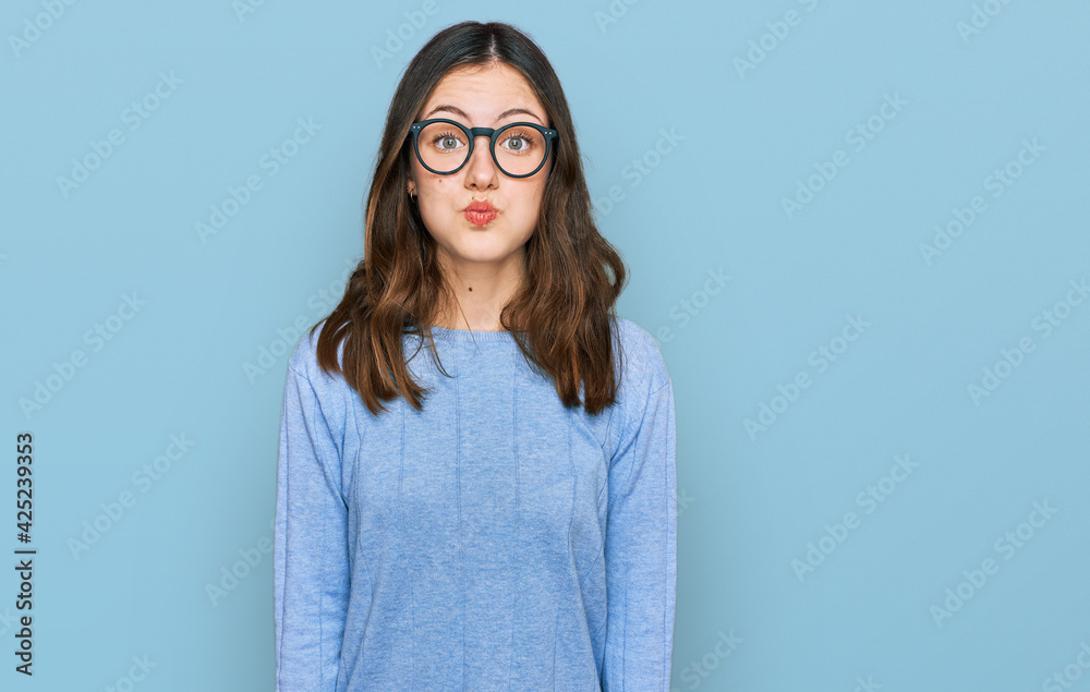 Young beautiful woman wearing casual clothes and glasses puffing cheeks with funny face. mouth inflated with air, crazy expression. Young beautiful woman wearing casual clothes and glasses puffing cheeks with funny face. mouth inflated with air, crazy expression.