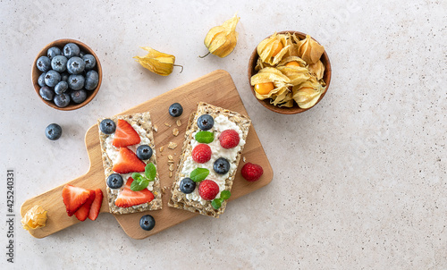 Rye oats crispbread with cottage cheese, mint leaves, fresh strawberries, and blueberries. Top view. Healthy food snack.