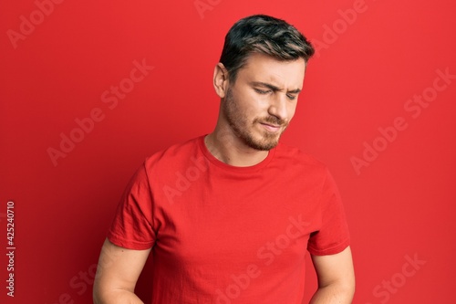 Handsome caucasian man wearing casual red tshirt with hand on stomach because indigestion, painful illness feeling unwell. ache concept.