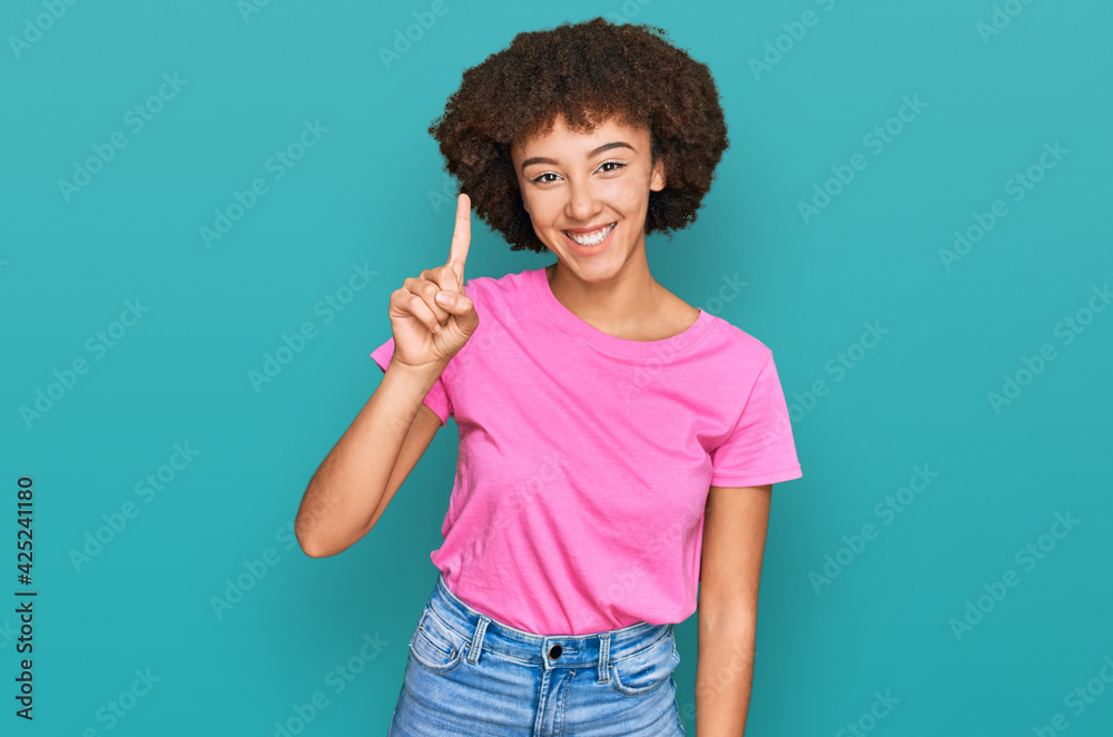 Young hispanic girl wearing casual clothes showing and pointing up with finger number one while smiling confident and happy. Young hispanic girl wearing casual clothes showing and pointing up with finger number one while smiling confident and happy.