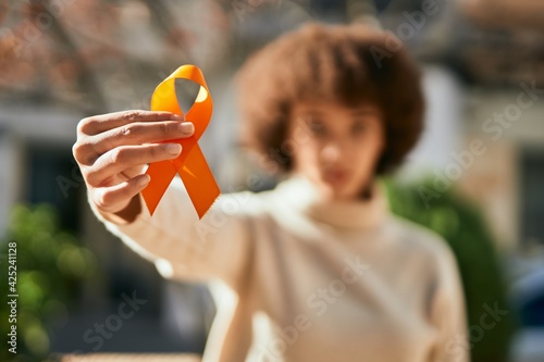 Schilderij op canvas Young hispanic girl with serious expression holding orange awareness ribbon at the city