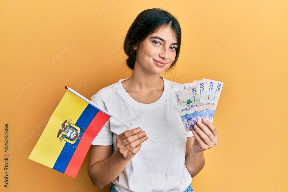 Young caucasian woman holding colombia flag and colombian pesos banknotes relaxed with serious expression on face. simple and natural looking at the camera. Young caucasian woman holding colombia flag and colombian pesos banknotes relaxed with serious expression on face. simple and natural looking at the camera.