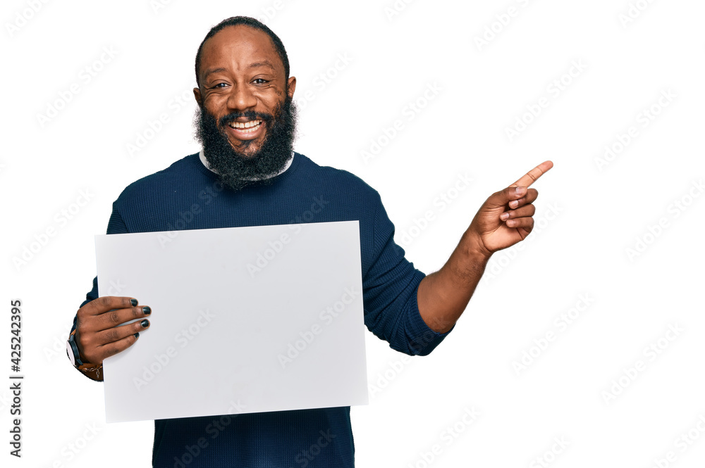 Young african american man holding blank empty banner smiling happy pointing with hand and finger to the side Young african american man holding blank empty banner smiling happy pointing with hand and finger to the side