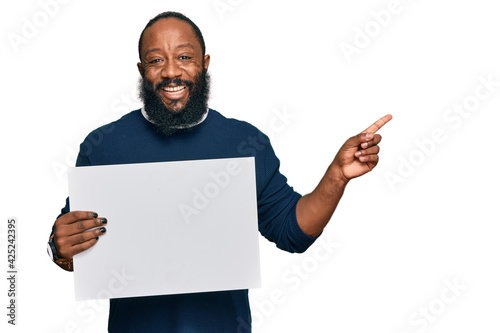 Young african american man holding blank empty banner smiling happy pointing with hand and finger to the side