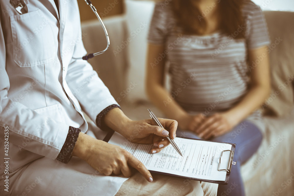 Obraz premium Unknown woman doctor and patient discussing current health examination while sitting in cozy living room. Stay at home concept during Coronavirus pandemic and self isolation quarantine