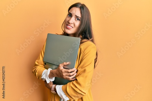 Young beautiful woman holding laptop clueless and confused expression. doubt concept.