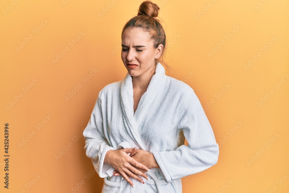 Young blonde woman wearing bathrobe with hand on stomach because indigestion, painful illness feeling unwell. ache concept. Young blonde woman wearing bathrobe with hand on stomach because indigestion, painful illness feeling unwell. ache concept.