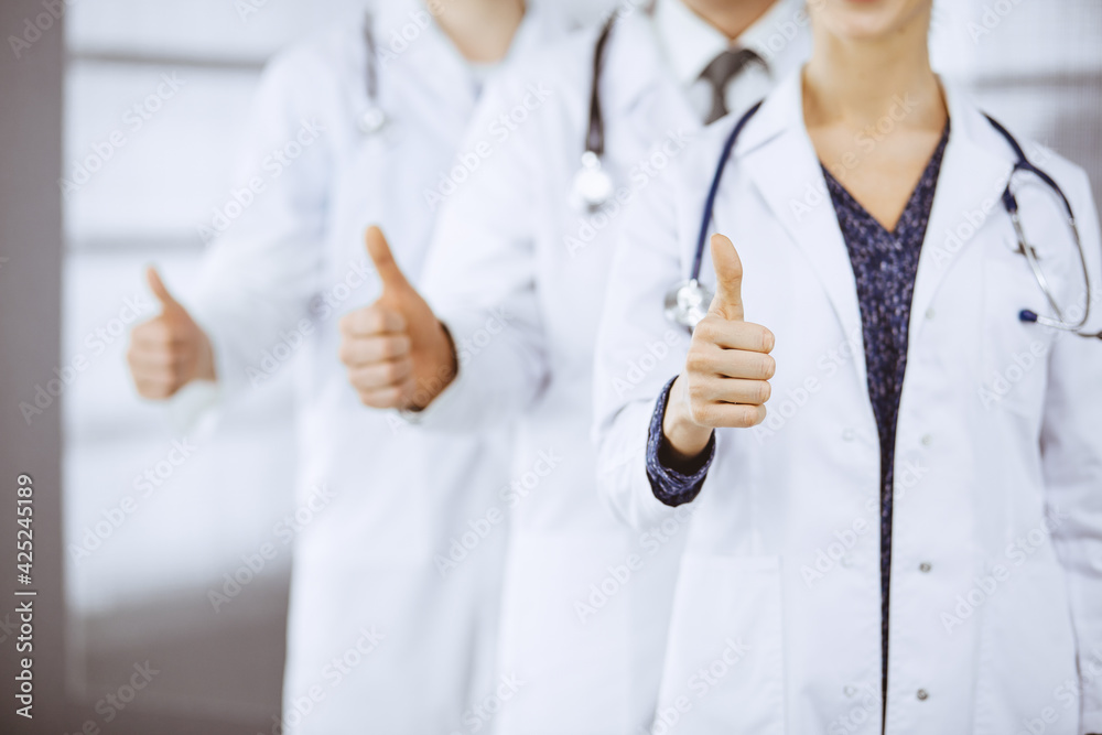 Doctors standing as a team with thumbs up in clinic and ready to help patients. Medical help, insurance and medicine concept Doctors standing as a team with thumbs up in clinic and ready to help patients. Medical help, insurance and medicine concept
