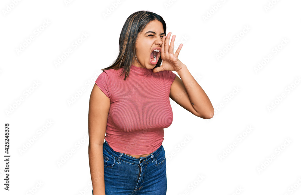 Young hispanic girl wearing casual t shirt shouting and screaming loud to side with hand on mouth. communication concept. Young hispanic girl wearing casual t shirt shouting and screaming loud to side with hand on mouth. communication concept.