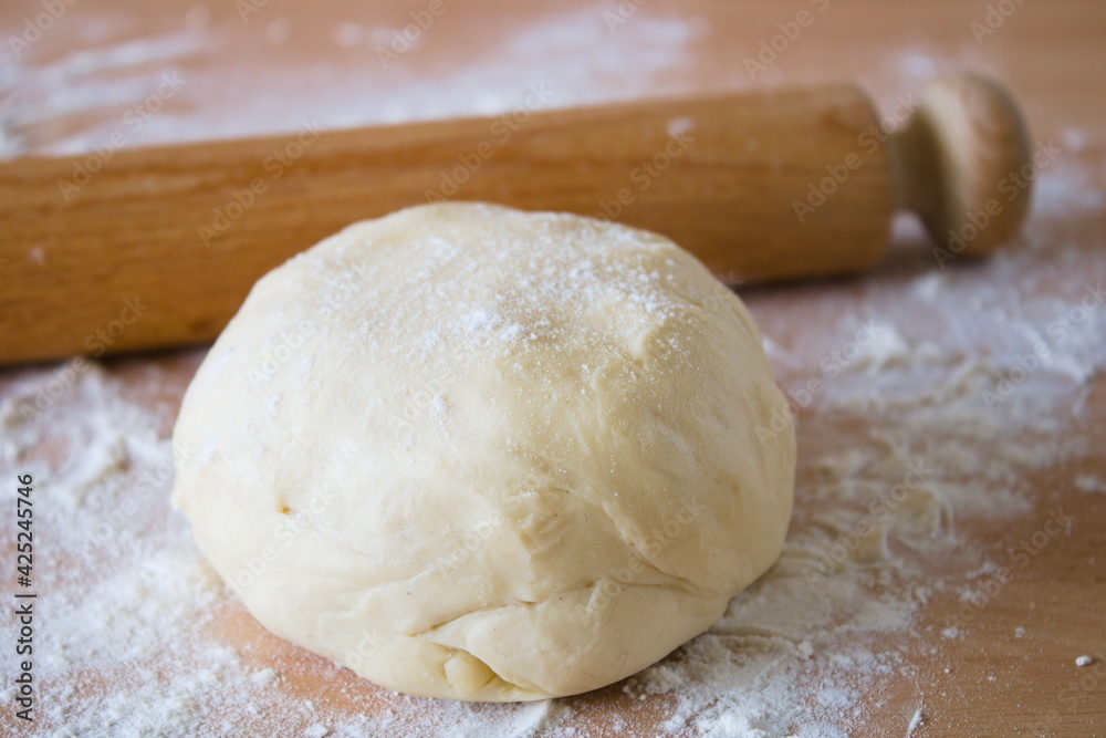 Ball of dough, pastry, on the wooden work top with scattered flour, rolling pin in the background Ball of dough, pastry, on the wooden work top with scattered flour, rolling pin in the background
