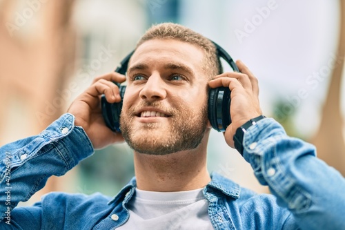 Young caucasian man smiling happy using headphones at the city.